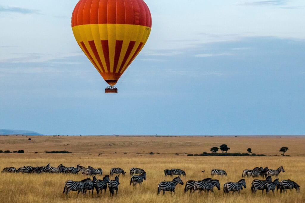 Hot air balloon floating over zebra herd Masai Mara Kenya safari
